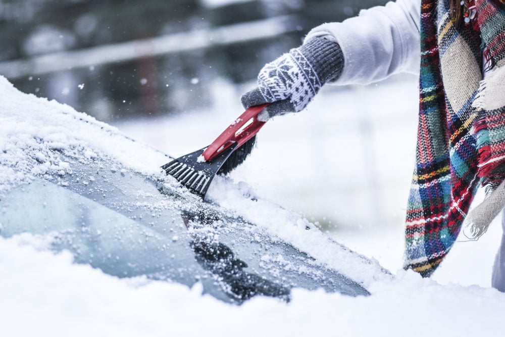 A driver scraping ice off their windshield before getting in the car.