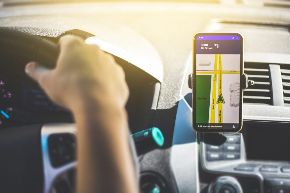 Point of view perspective of a driver with GPS on their smartphone next to the wheel.