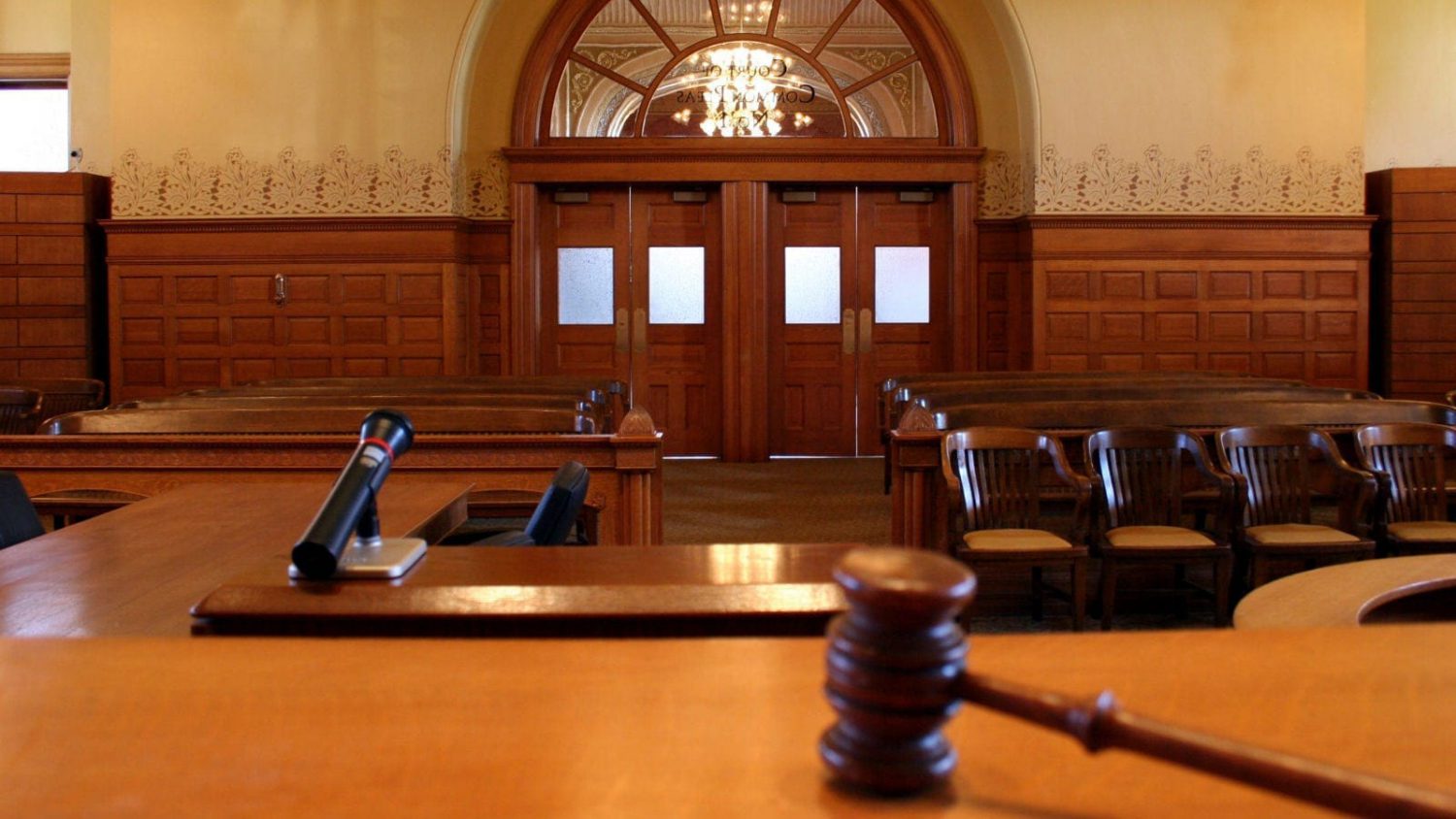Empty courtroom with a gavel and witness box in the foreground.