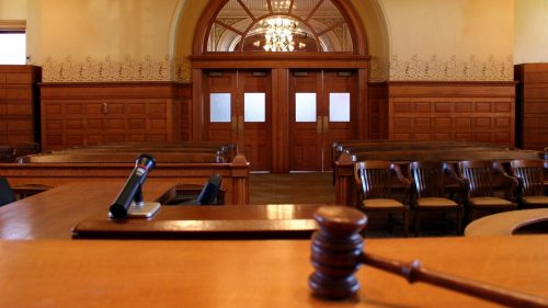 Empty courtroom with a gavel and witness box in the foreground.