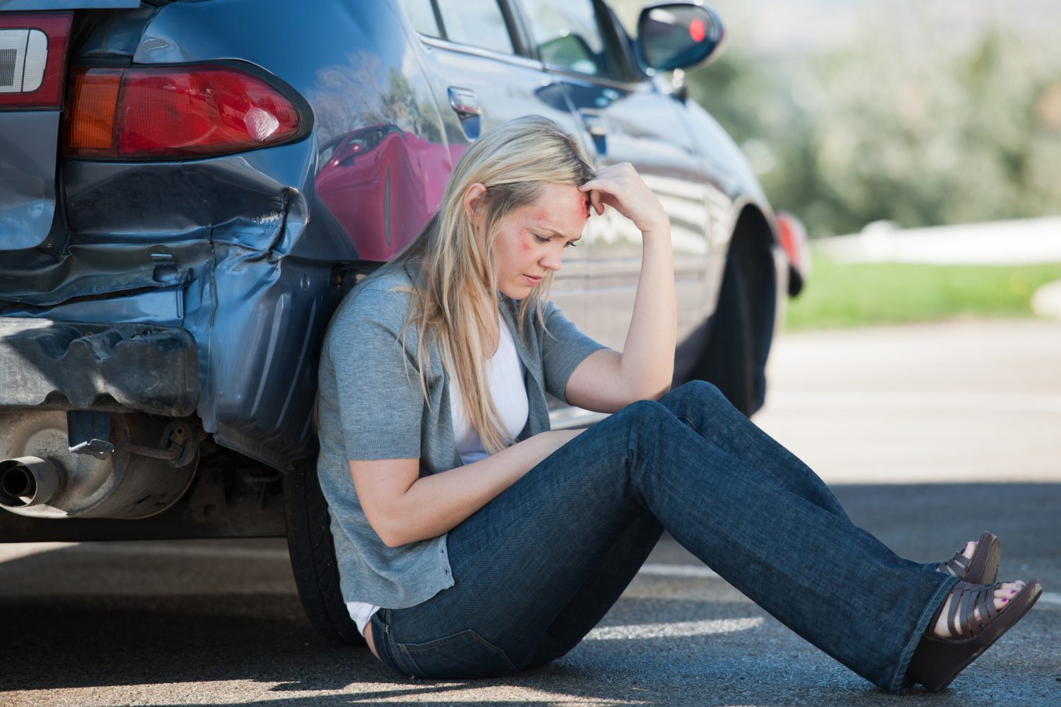 A woman leaning against her car after being injured in a Fort Wayne car accident.