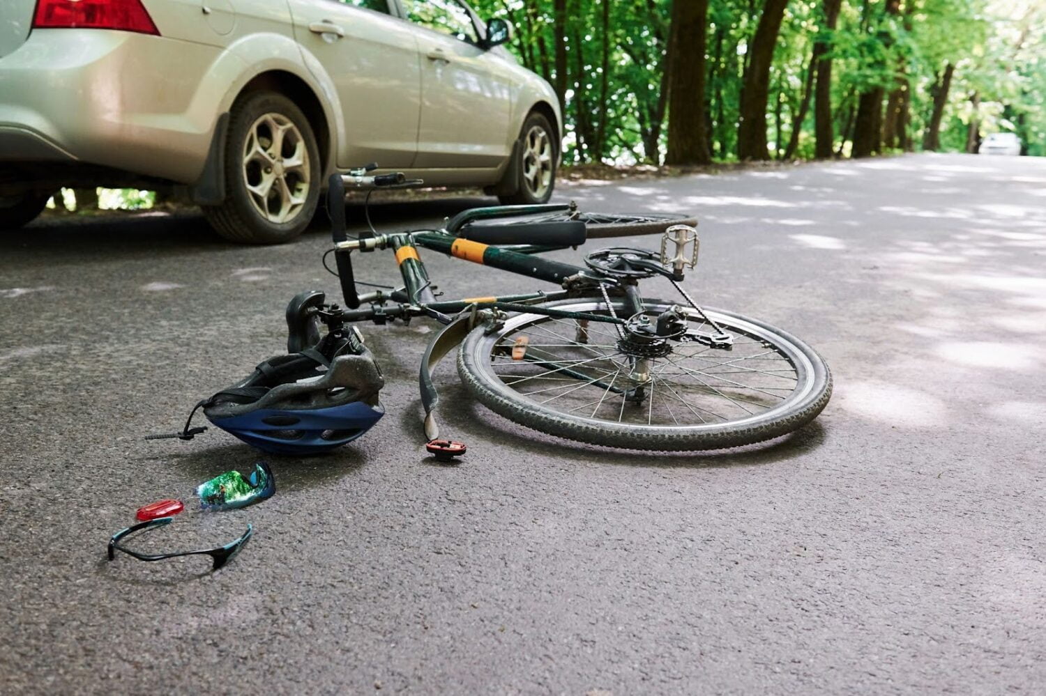 A bicycle and helmet with shattered visor lay in the street beside a white sedan.