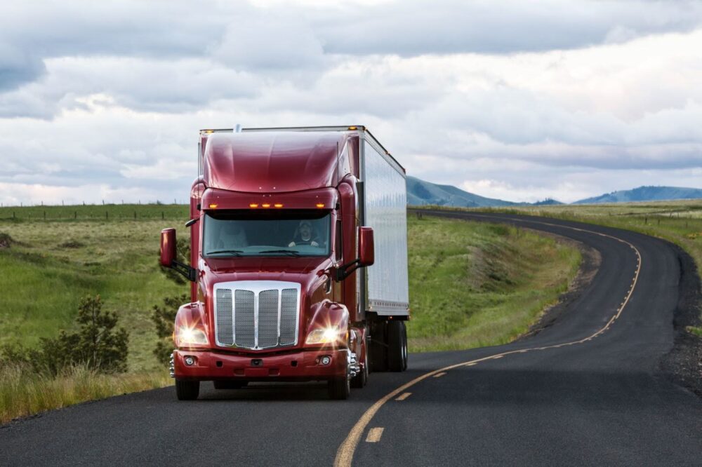 A red semi-truck driving on a rural highway.