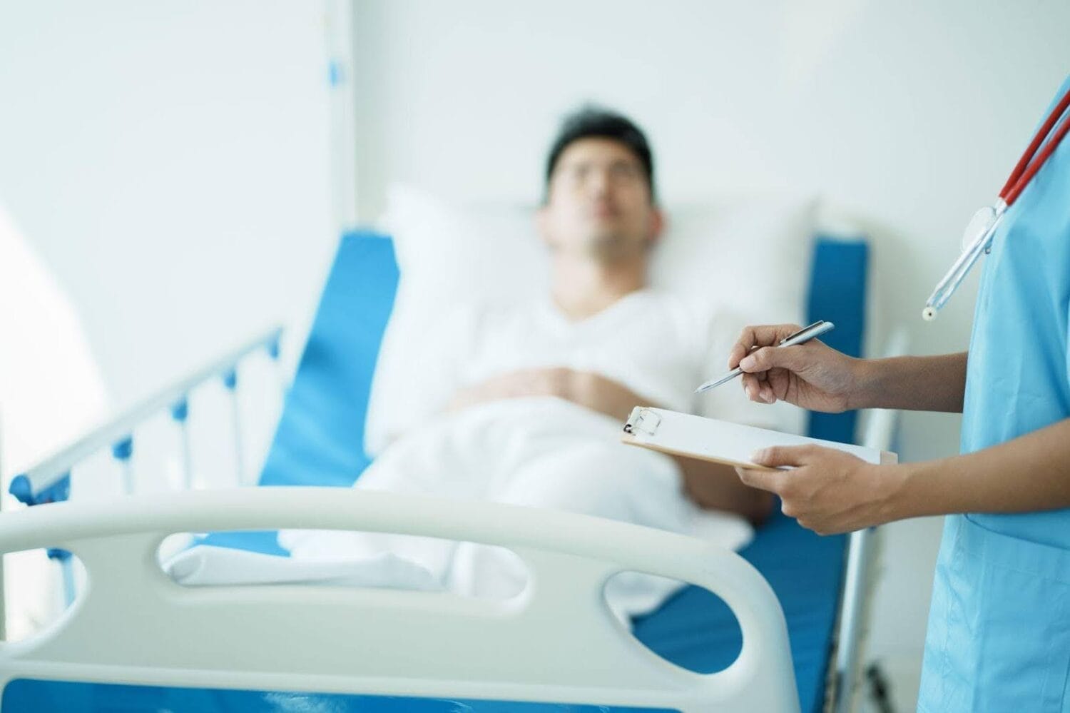 Close up of a doctor holding a clipboard beside a patient in a hospital bed.
