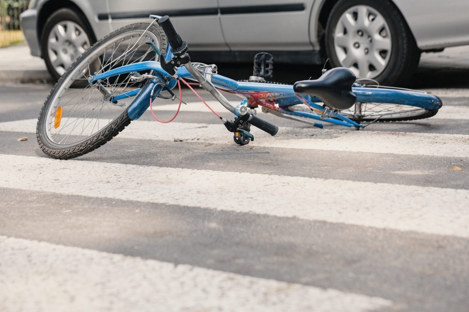 A blue bicycle lies in the middle of the street beside a gray sedan.
