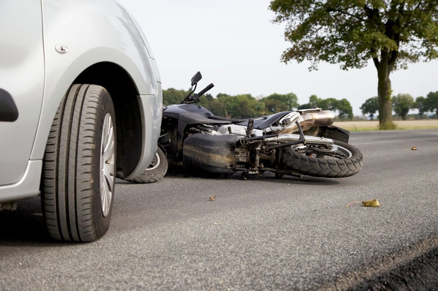 A motorcycle lying on its side on the road in front of a car after an accident.