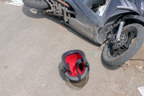 A motorcycle lying on its side on dirty pavement with a helmet next to it.
