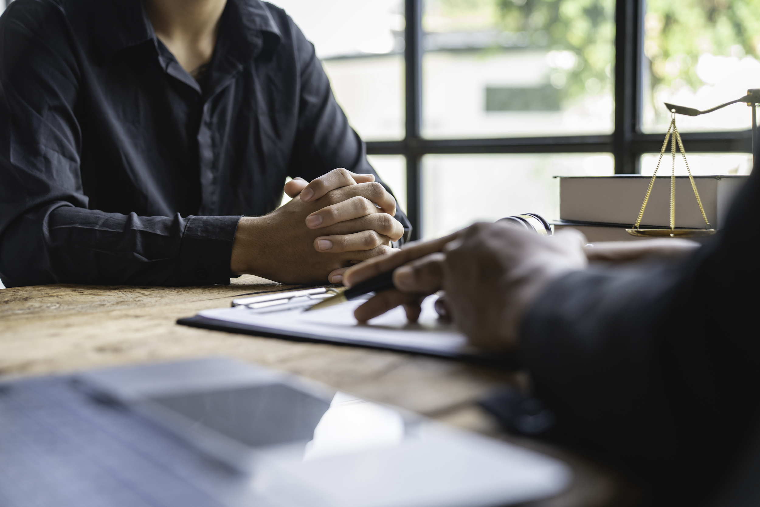 A cropped image of a person consulting with a lawyer as they sit at a wooden desk.