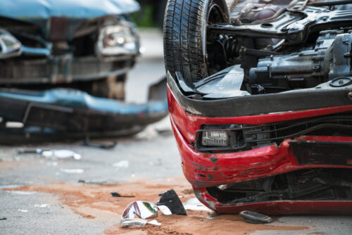 Wrecked cars after an accident. A black car with a bumper hanging off its front, and an overturned red car.