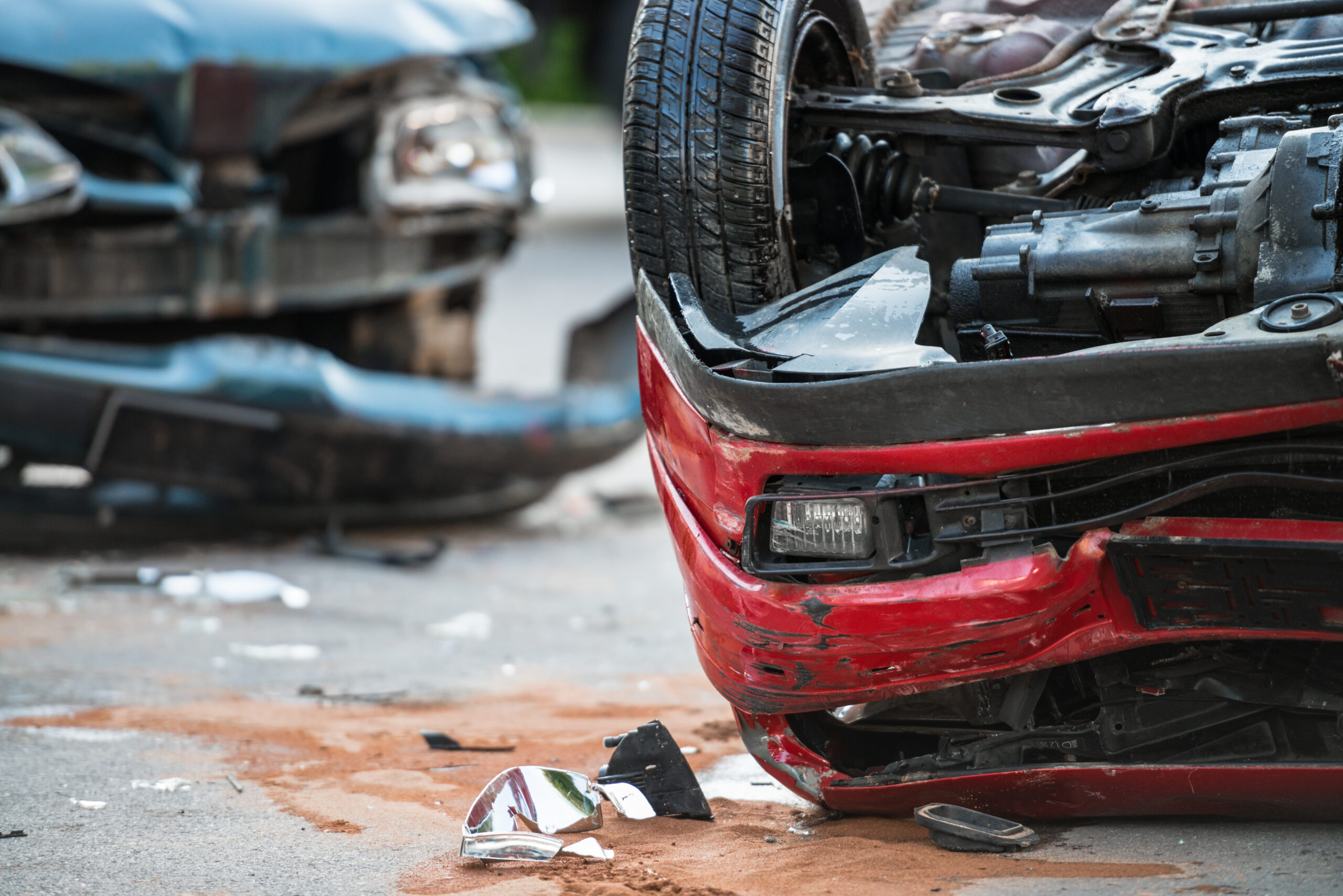 Wrecked cars after an accident. A black car with a bumper hanging off its front, and an overturned red car.