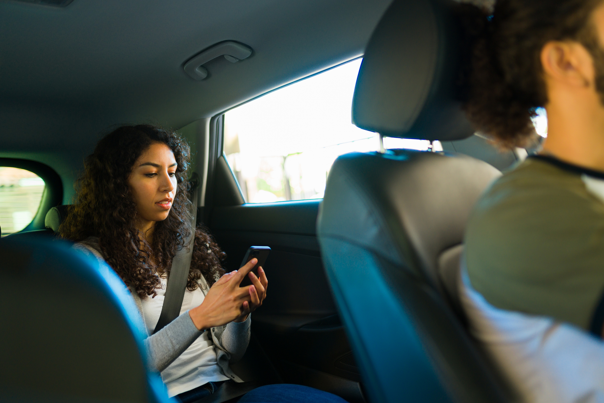Uber passenger looking at her smartphone while riding in the back seat of a car.