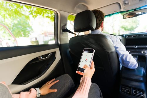 Uber passenger using a smartphone while riding in the back seat of a car with a rideshare driver.